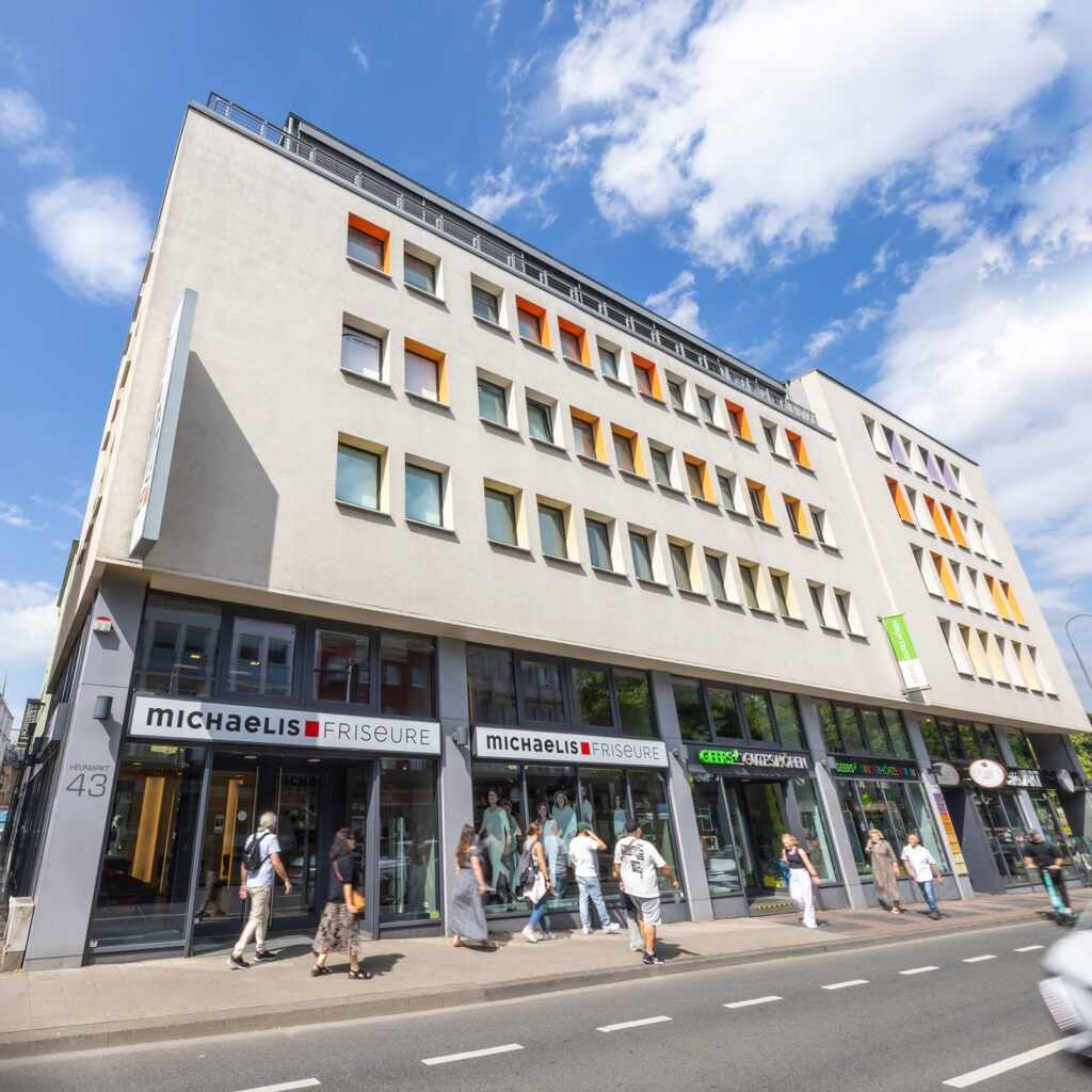 Die Außenansicht zeigt den Salon Michaelis Friseure in Köln City am Heumarkt in zentraler Innenstadtlage. Die gut sichtbare Fassade mit Schaufenstern und Eingangsbereich fügt sich in das urbane Umfeld ein und macht den Salon als festen Bestandteil des Stadtbildes klar erkennbar.