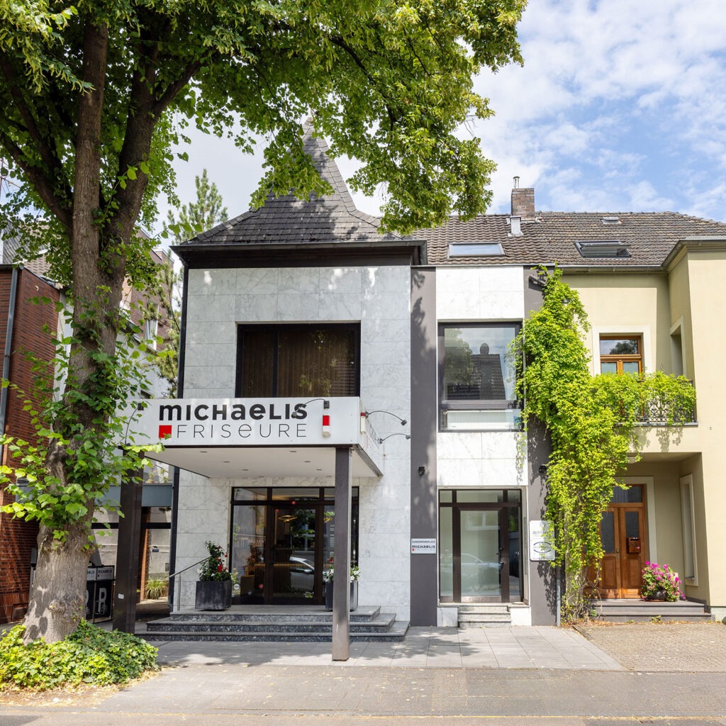 Außenansicht des Salons Michaelis Friseure in Köln-Weiden mit markantem Eingang und grüner Wohnstraßenlage