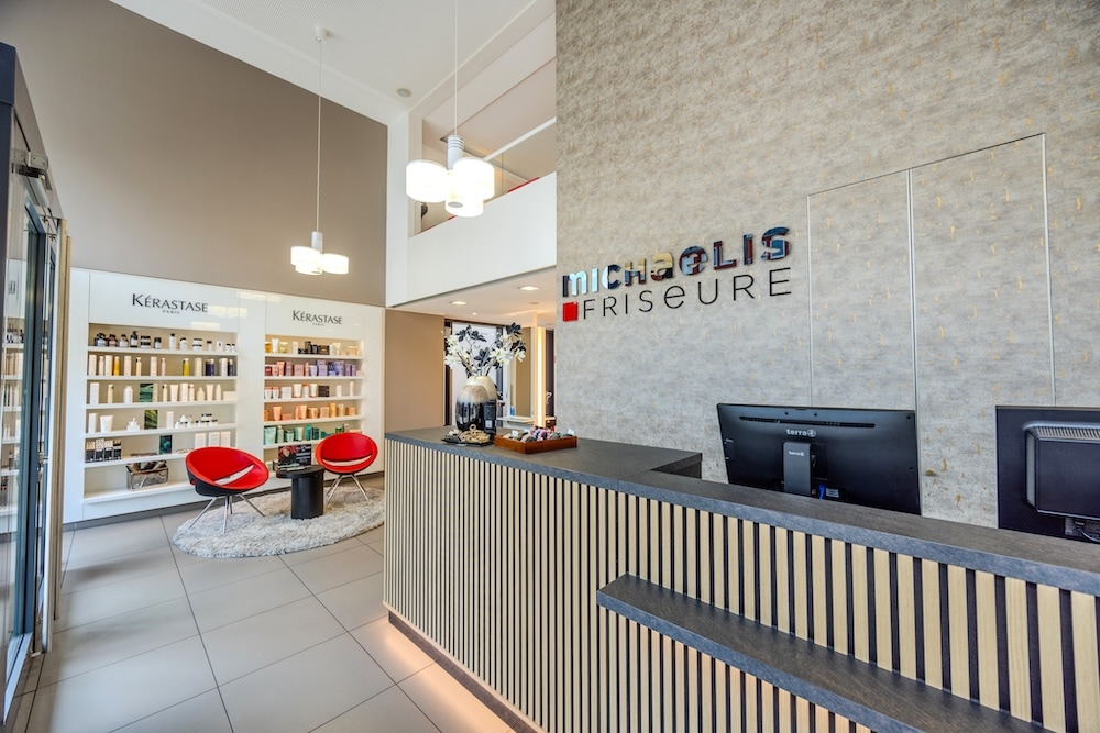 Empfangsbereich von Michaelis Friseure in Köln mit moderner Theke, Logo-Wand und hochwertiger Salonarchitektur