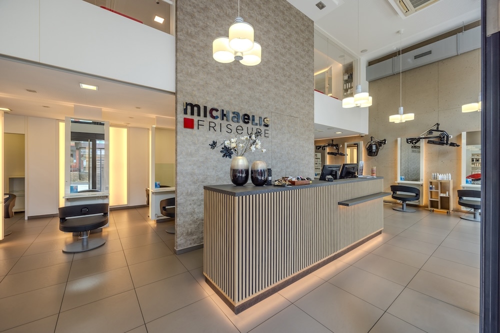 Großzügiger Salon von Michaelis Friseure mit Empfangstheke, Logo-Wand, Stylingplätzen und moderner Innenarchitektur