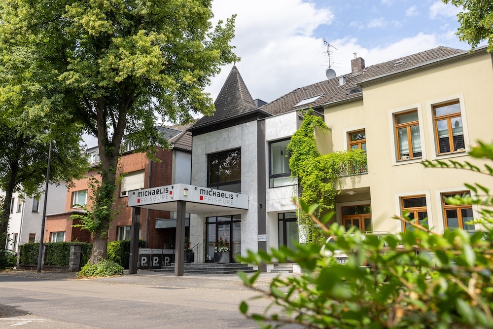 Außenansicht des Salons Michaelis Friseure in Köln-Weiden mit markantem Eingang und grüner Wohnstraßenlage